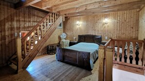 Un dormitorio de cabaña de madera con cama, mesita de noche, cómoda, ventilador y escalera.
