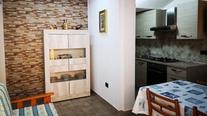Une cuisine de taille réduite avec un mur en pierre, des placards en bois et un coin repas comprenant une table et des chaises.