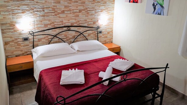 Un lit bien fait, avec du linge de lit blanc et une couvre-lit rouge, une table de chevet en bois et un mur décoré d’un motif en briques.