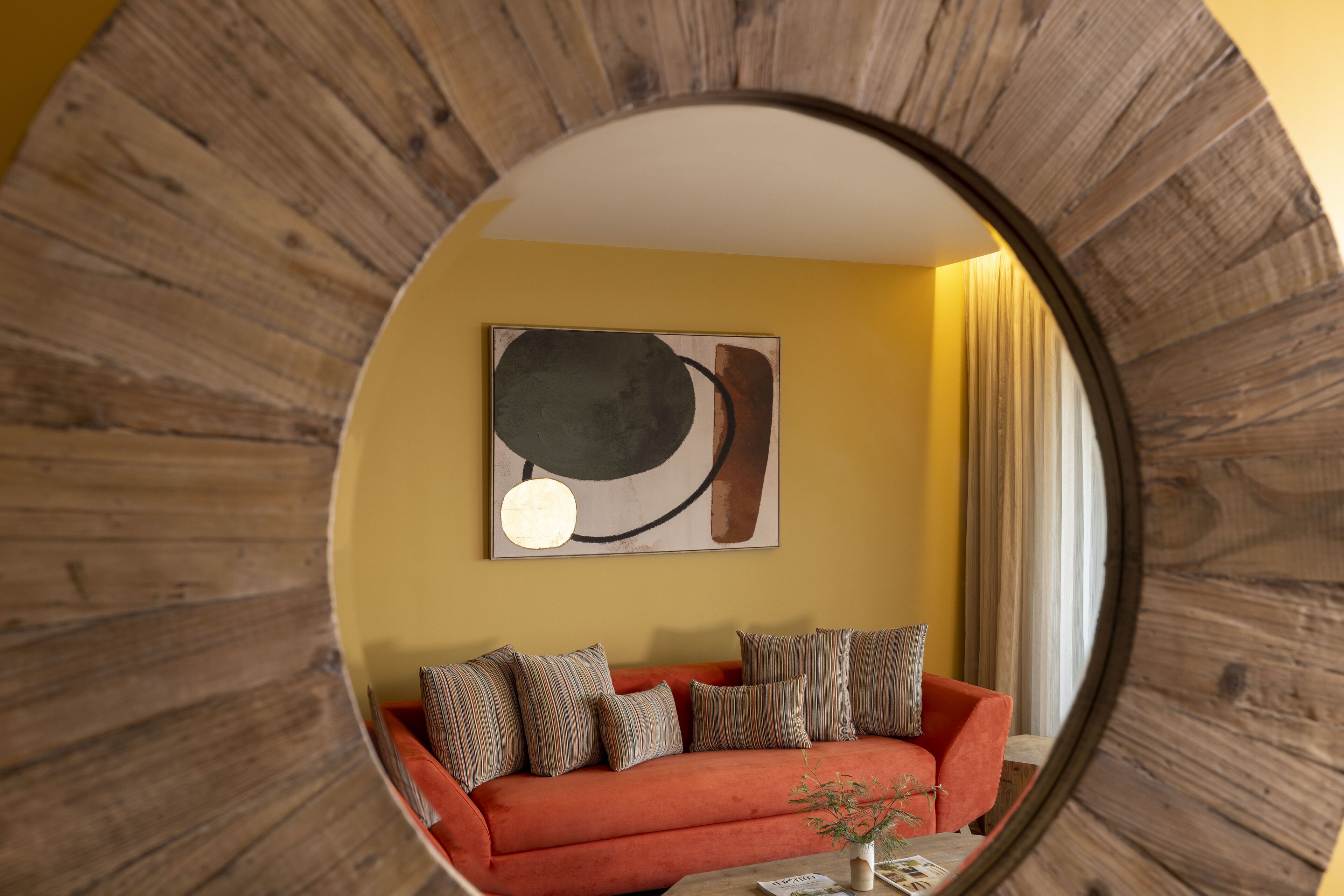 Une pièce avec un miroir rond, un canapé rouge et un tableau accroché au mur.