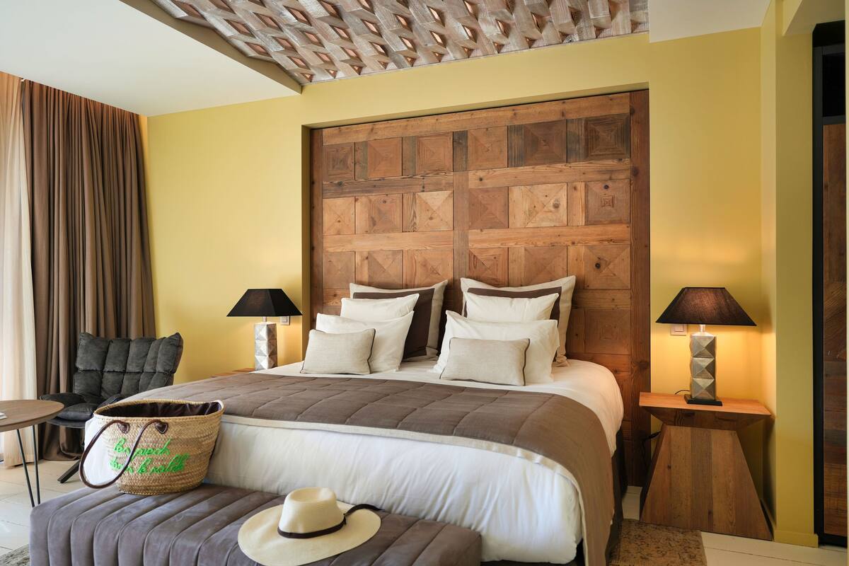 A bedroom with a large bed, two bedside tables with lamps, a chair, and a decorative wall panel.