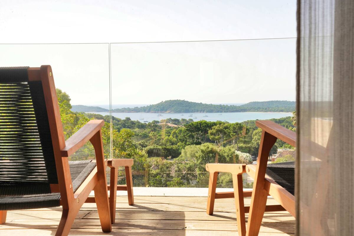 A wooden deck with two chairs and a table overlooking a scenic view of a lake and hills.