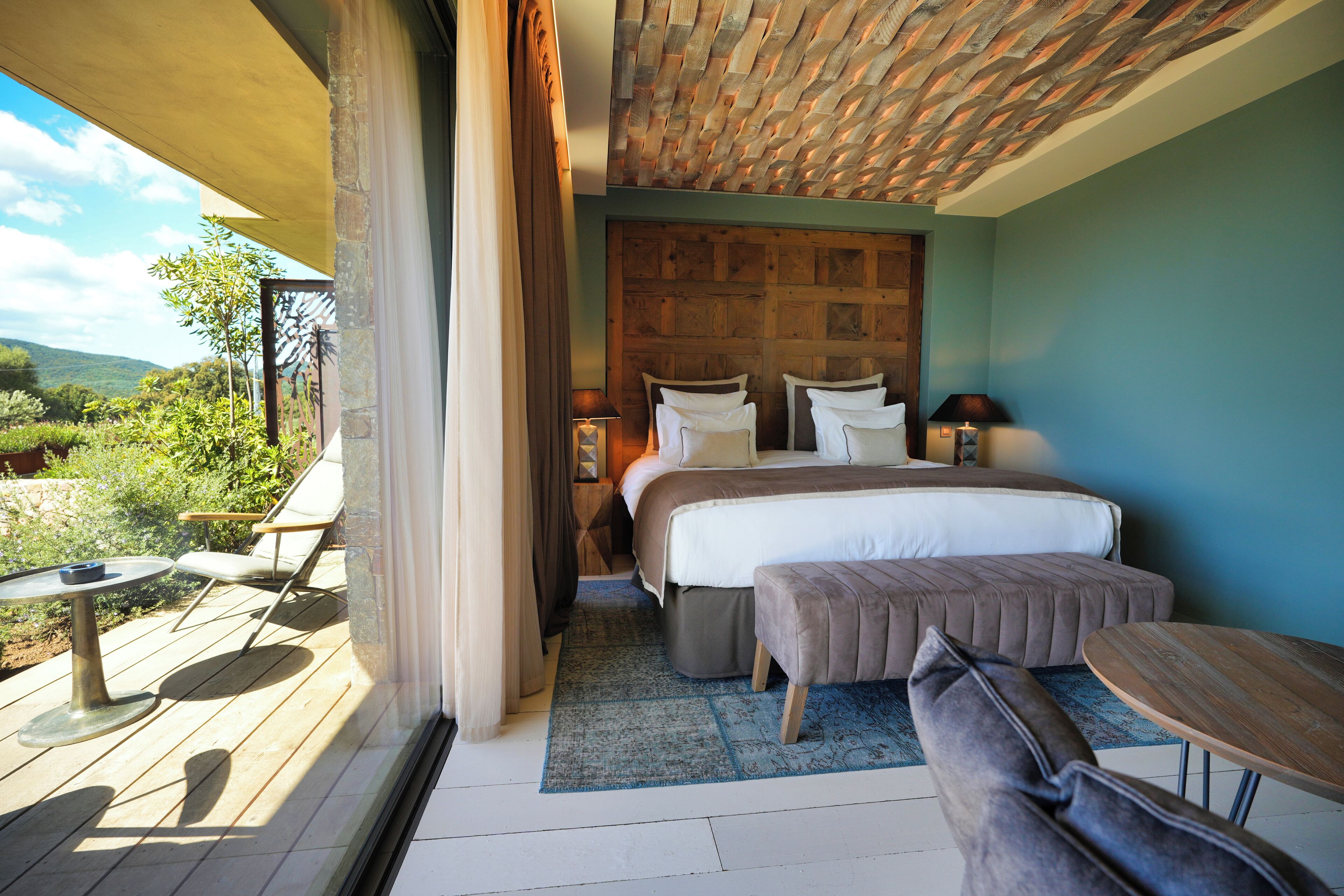 Ein Schlafzimmer mit einem großen Bett, Holzboden, Blick ins Freie und einem Balkon mit Tisch und Stühlen.
