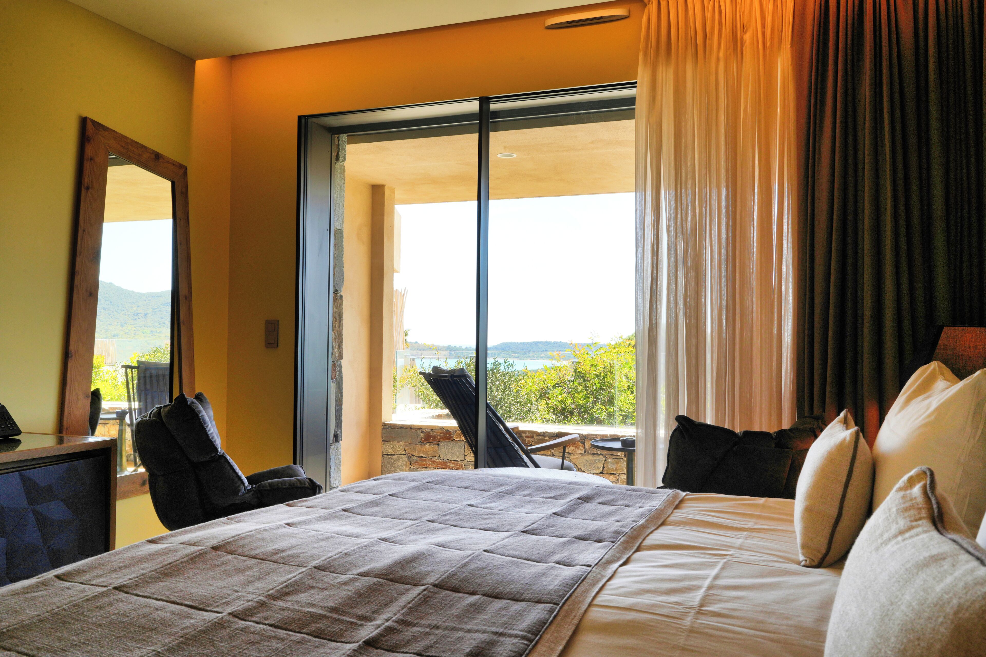 A hotel room with a bed, a chair, a desk, and a large window with a view.
