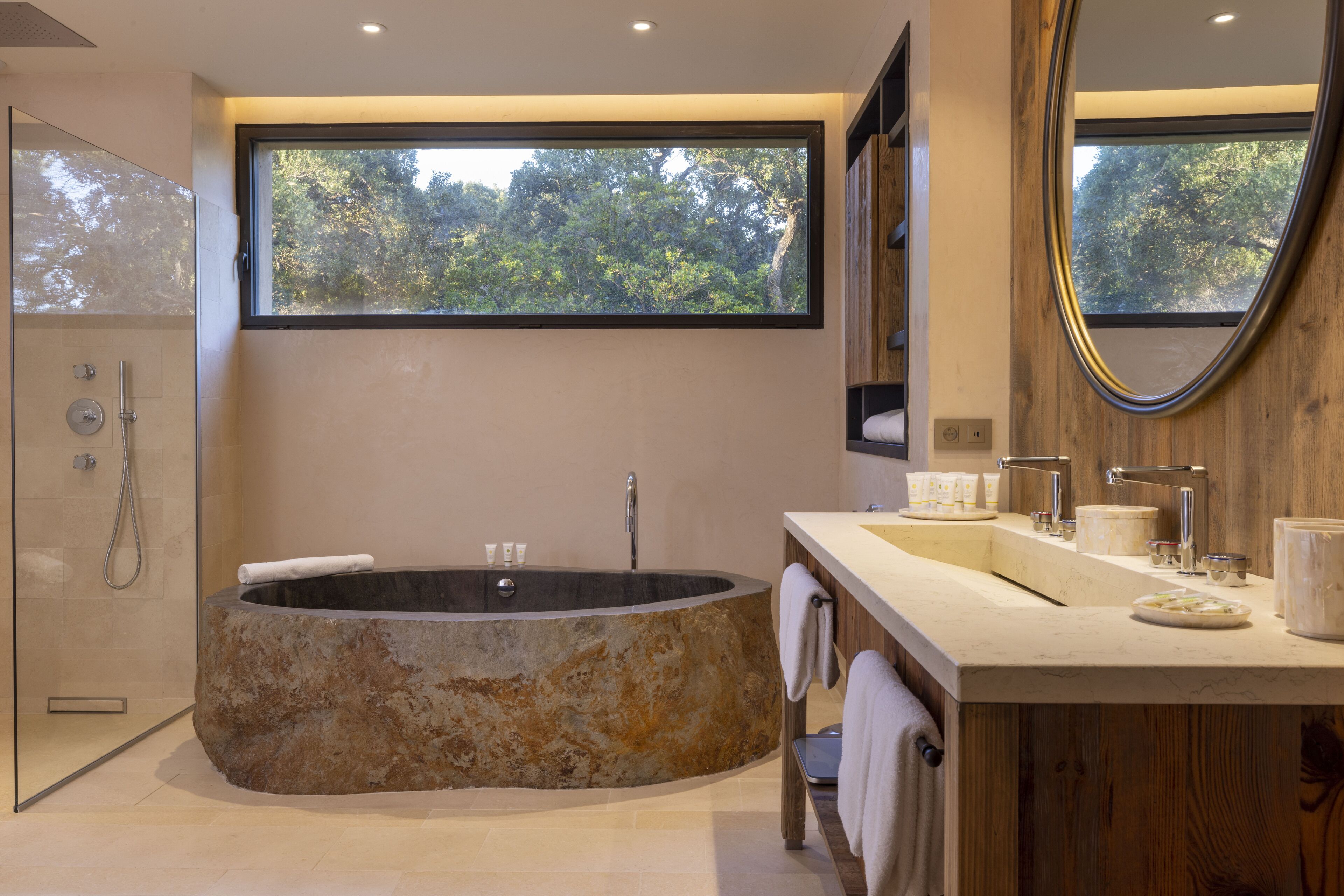 Un baño moderno con una bañera independiente, un espejo grande y una ventana que ofrece vistas a árboles.