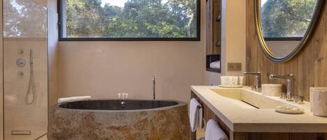 Un baño moderno con una bañera independiente, un espejo grande y una ventana que ofrece vistas a árboles.