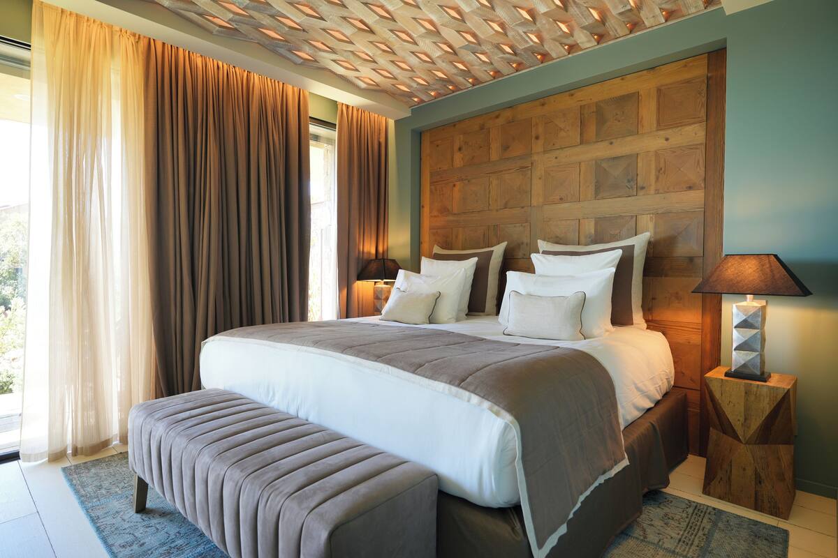 A large bed with a wooden headboard, a bench, and a nightstand with a lamp.