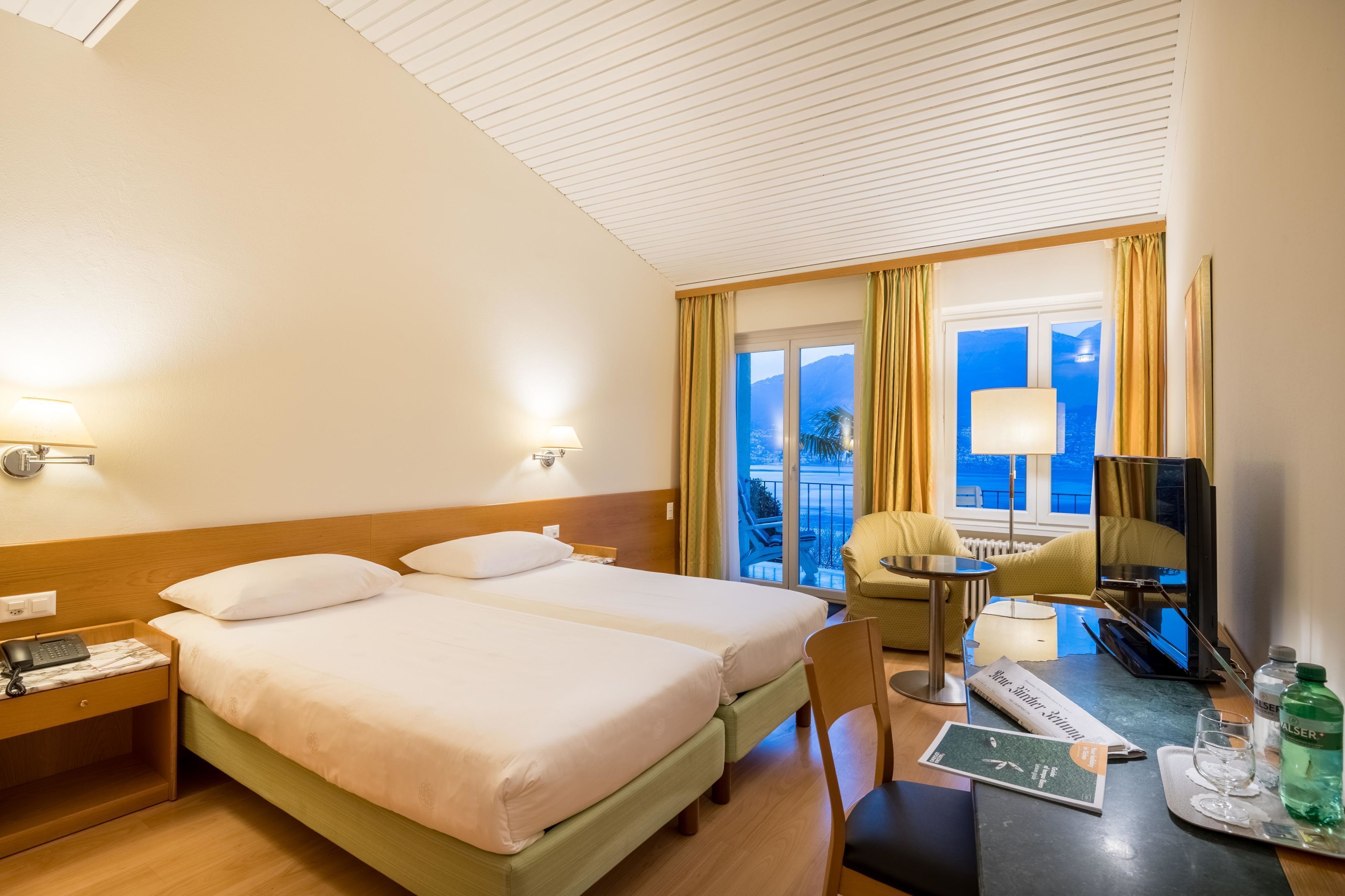 Habitación de hotel con dos camas, un escritorio, una silla, un televisor y vista al mar.