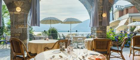 A restaurant with stone arches, outdoor seating, and umbrellas overlooking a scenic view.