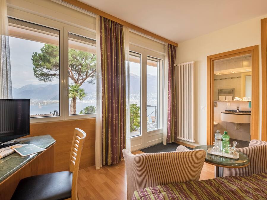 Habitación de hotel con televisión, escritorio, silla, sofá y vistas al mar y las montañas.