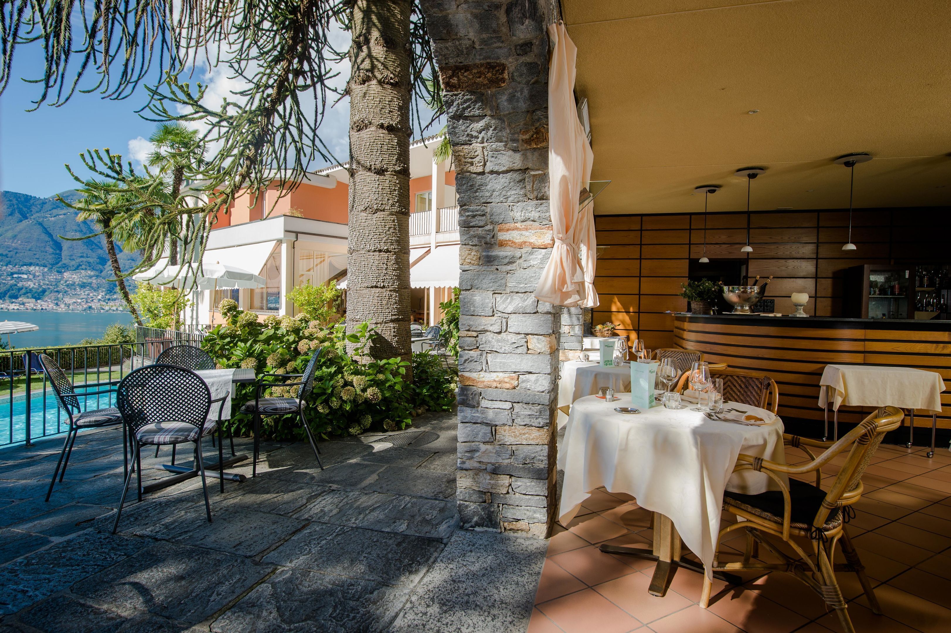 Un área de comedor al aire libre con mesas y sillas, una piscina y vistas al mar y a las montañas.