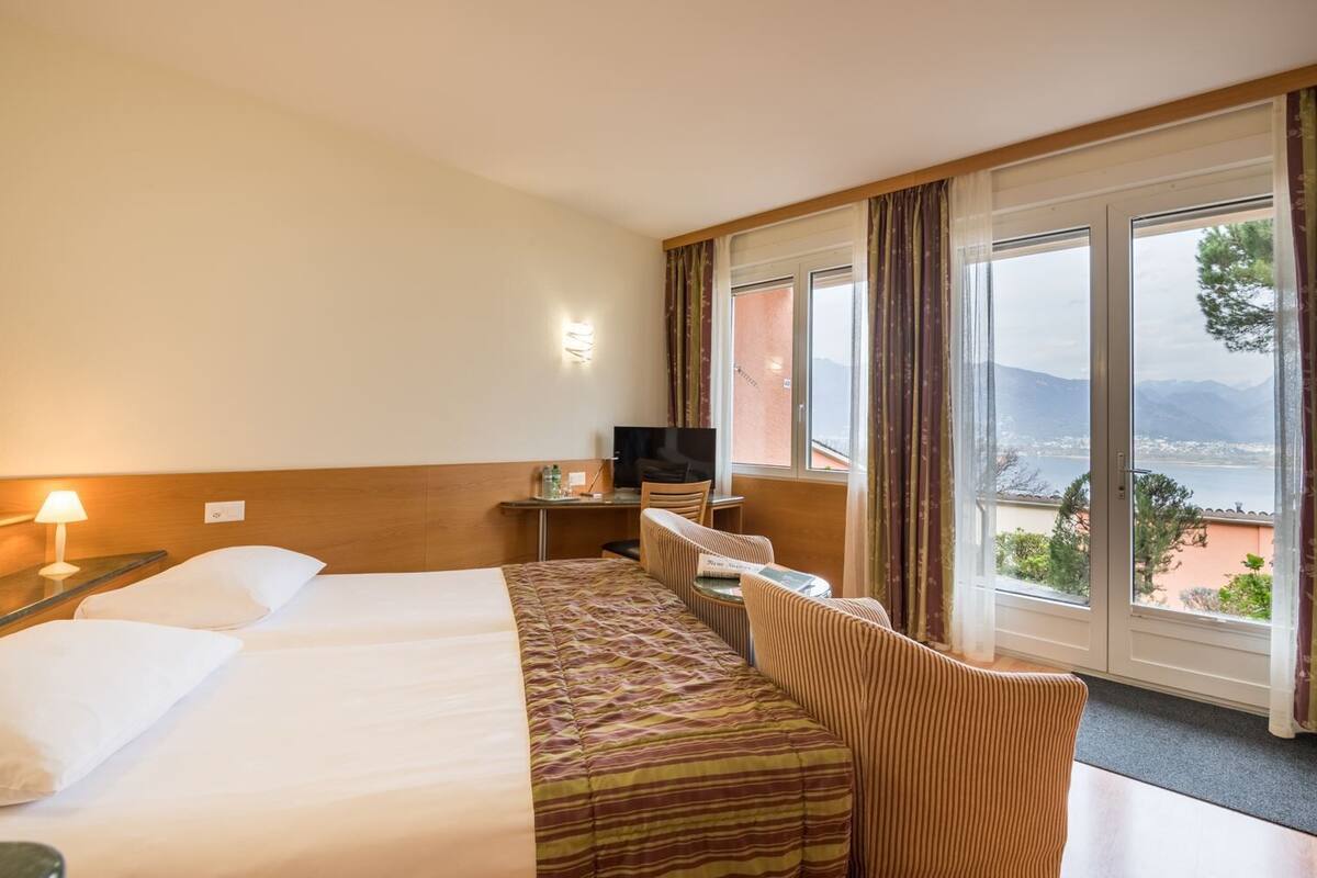 Habitación de hotel con dos camas, un escritorio con televisor y vista a un lago y montañas.