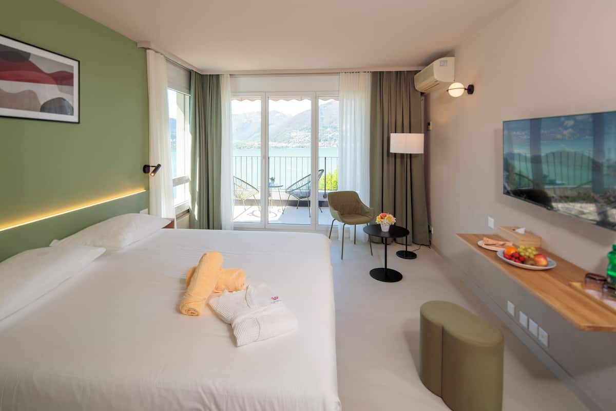 Habitación de hotel con una cama grande, una mesita con fruta, una silla y vistas a la montaña desde la ventana.