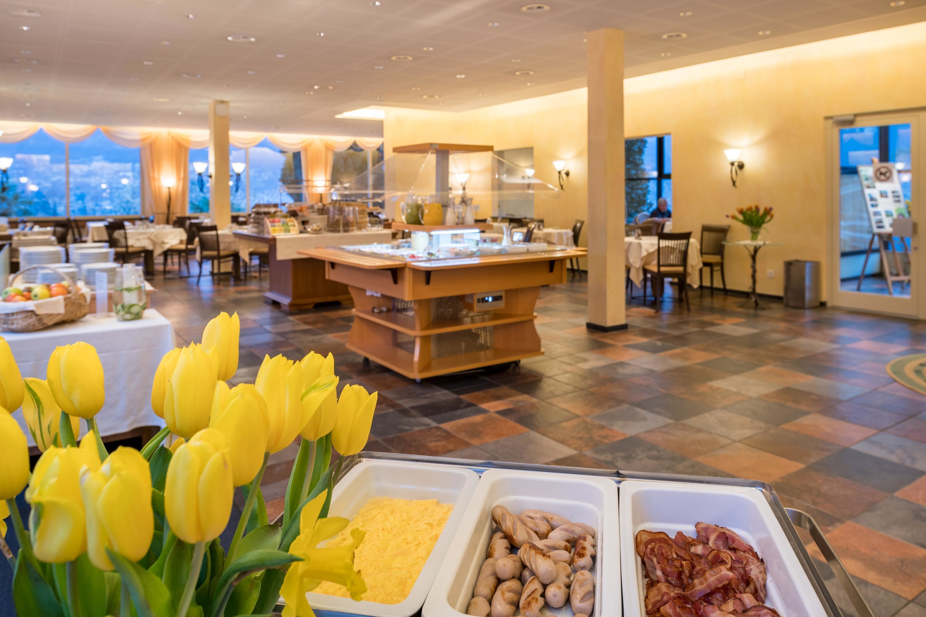 A buffet area with food options, a view of the city, and a decorative flower arrangement.