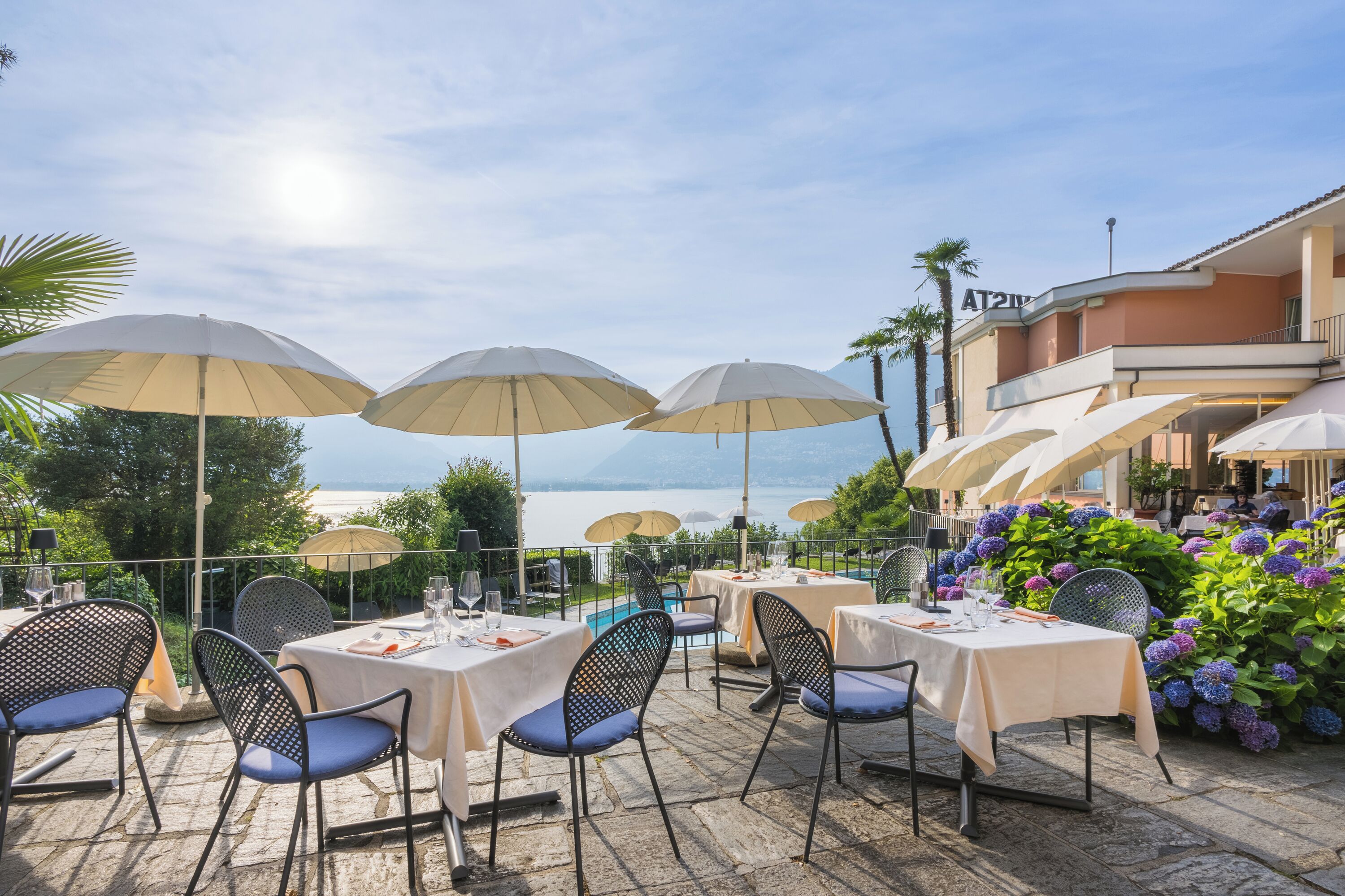 Un área de comedor al aire libre con mesas y sillas, sombrillas y vista al mar.