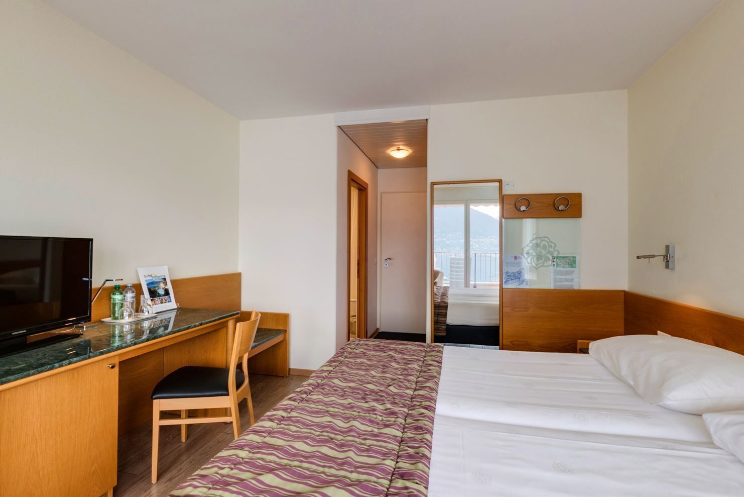 Une chambre d’hôtel avec un lit, un bureau et une chaise, une télévision et une vue sur l’extérieur.