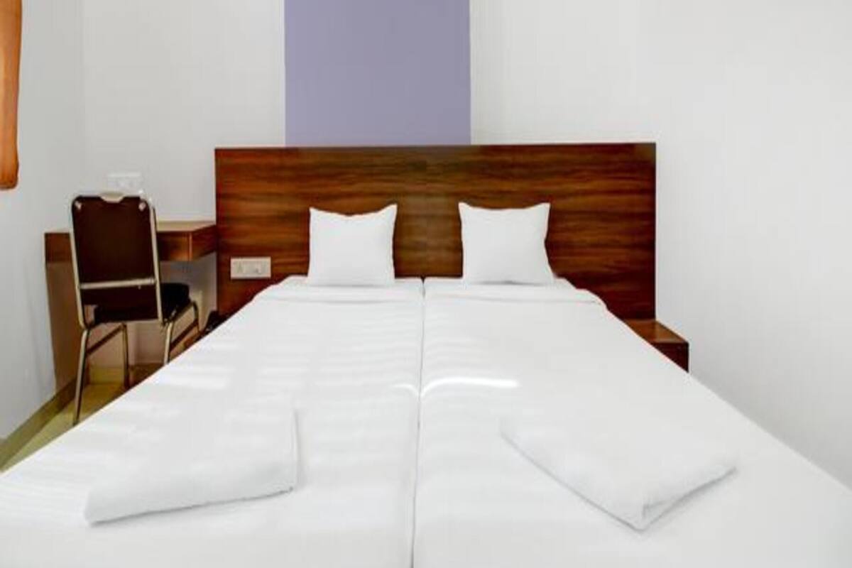 Una cama doble con sábanas blancas, un cabecero de madera y un pequeño escritorio con una silla.