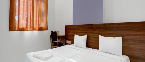 A neatly made bed with white linens and pillows, a wooden headboard, and a window with orange curtains.