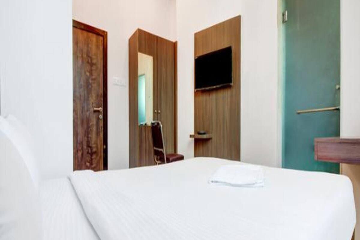 Habitación de hotel con una cama grande, una puerta de madera, un televisor montado en la pared y un baño con puerta verde.