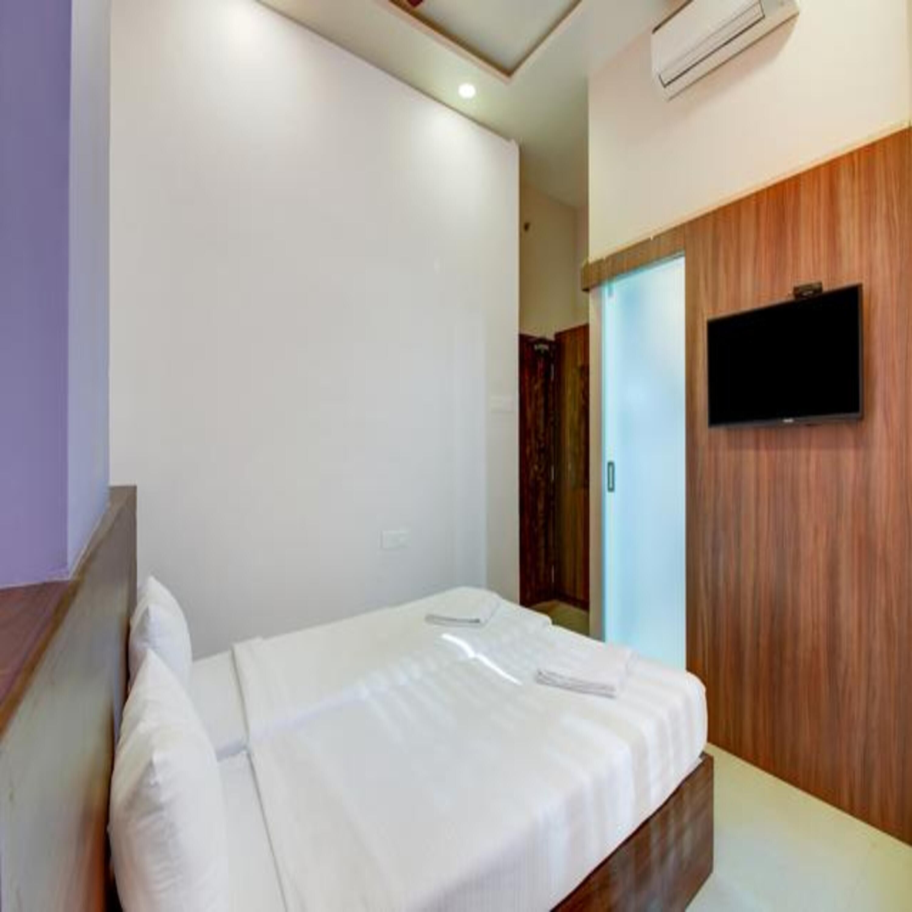 A hotel room with a bed, a flat-screen TV mounted on the wall, and a wooden panel design on the wall.