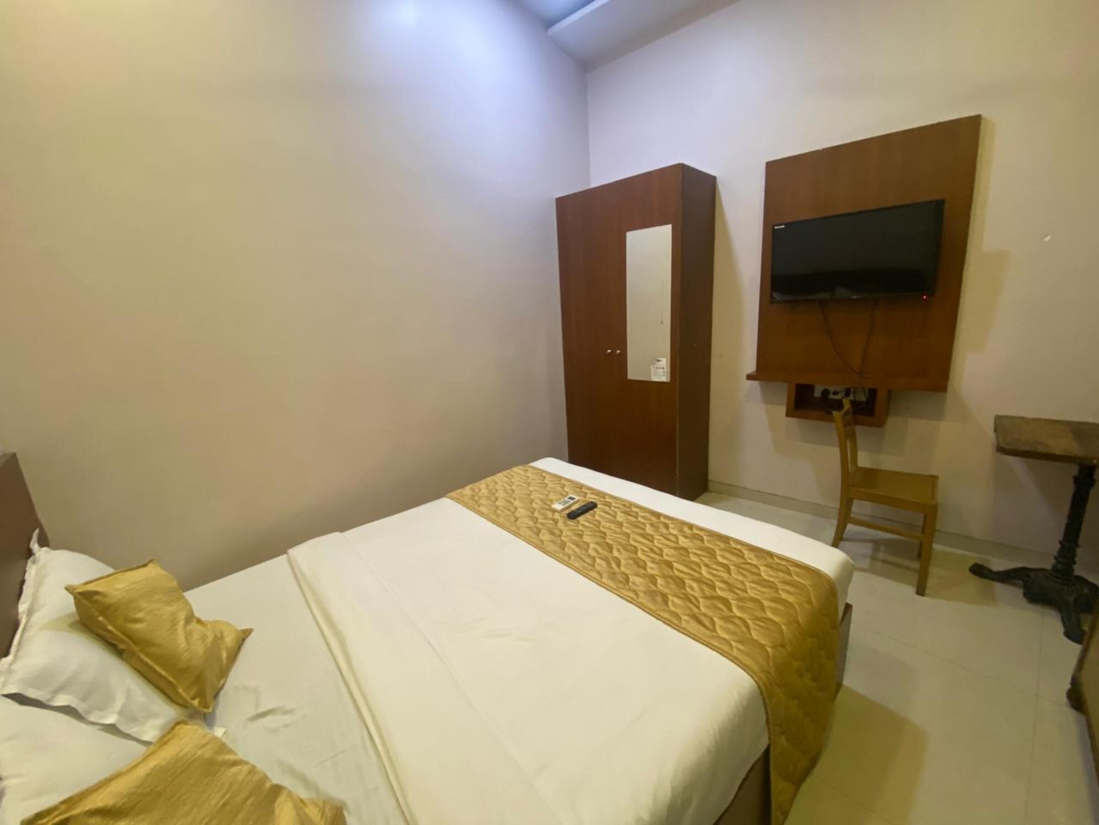 A hotel room with a bed, a TV mounted on the wall, and a wooden wardrobe.