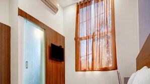 Una habitación de hotel con cama, televisión en la pared y ventana con cortinas.