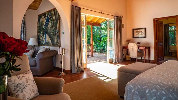 A cozy room with a sofa, a chair, a bed, and a desk. There is a painting on the wall and a window with curtains. - Karen Blixen Coffee Garden & Cottages (Nairobi)