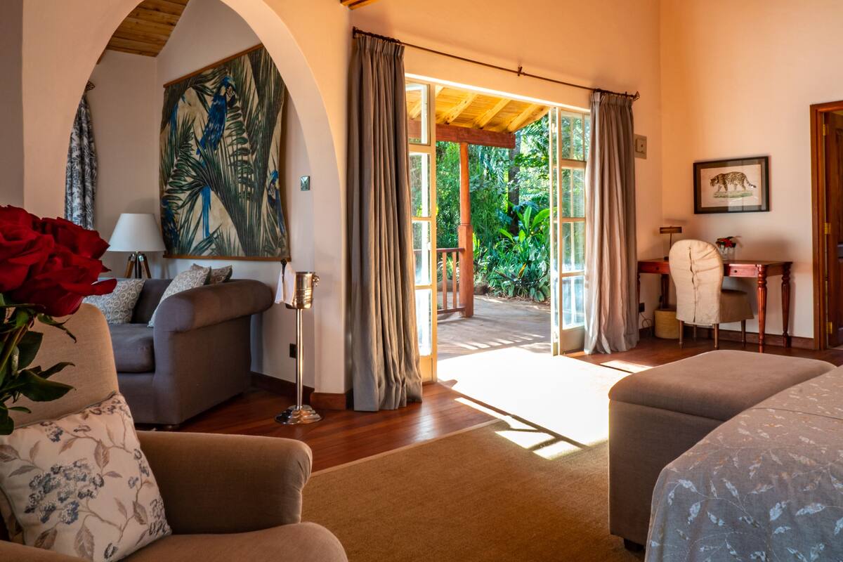 A cozy room with a sofa, a chair, a bed, and a desk. There is a painting on the wall and a window with curtains.