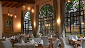 A dining area with patterned chairs, tables set with napkins, and hanging pendant lights. - Karen Blixen Coffee Garden & Cottages (Nairobi)