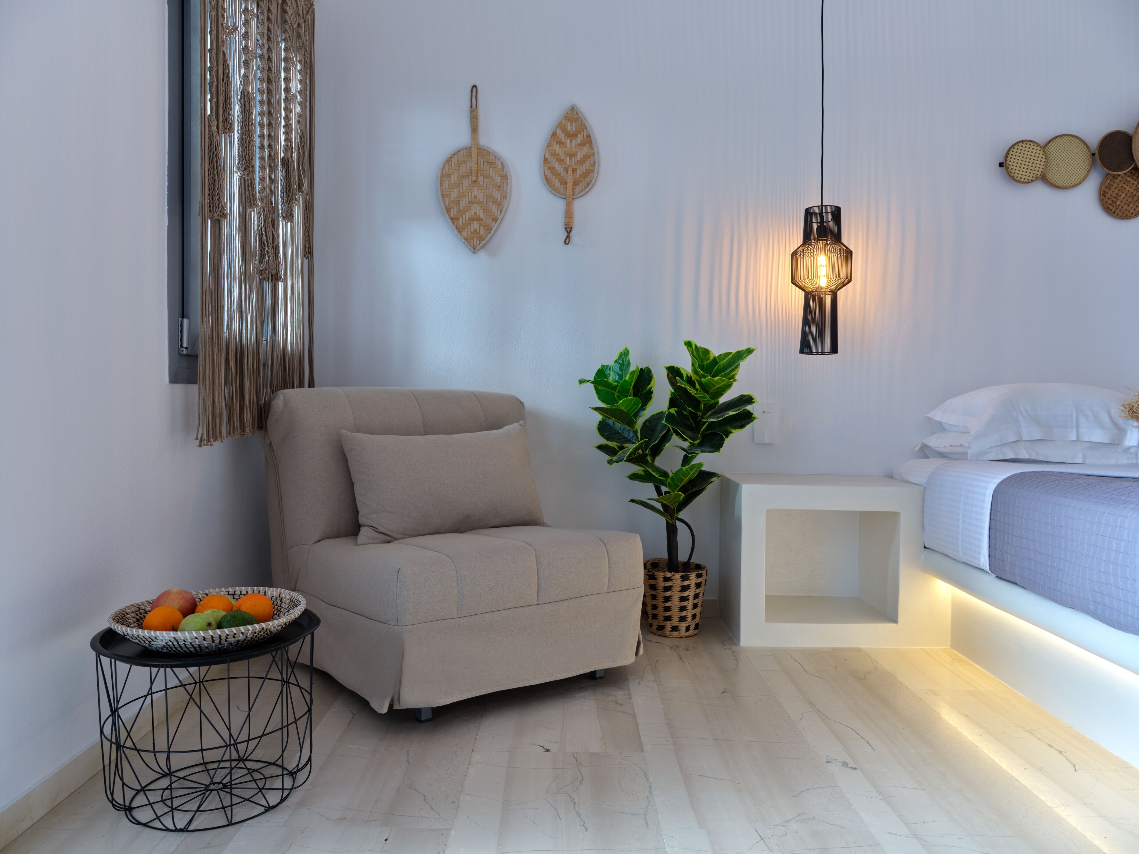 A modern bedroom with a sofa, a bedside table with a lamp, a potted plant, and a fruit basket.