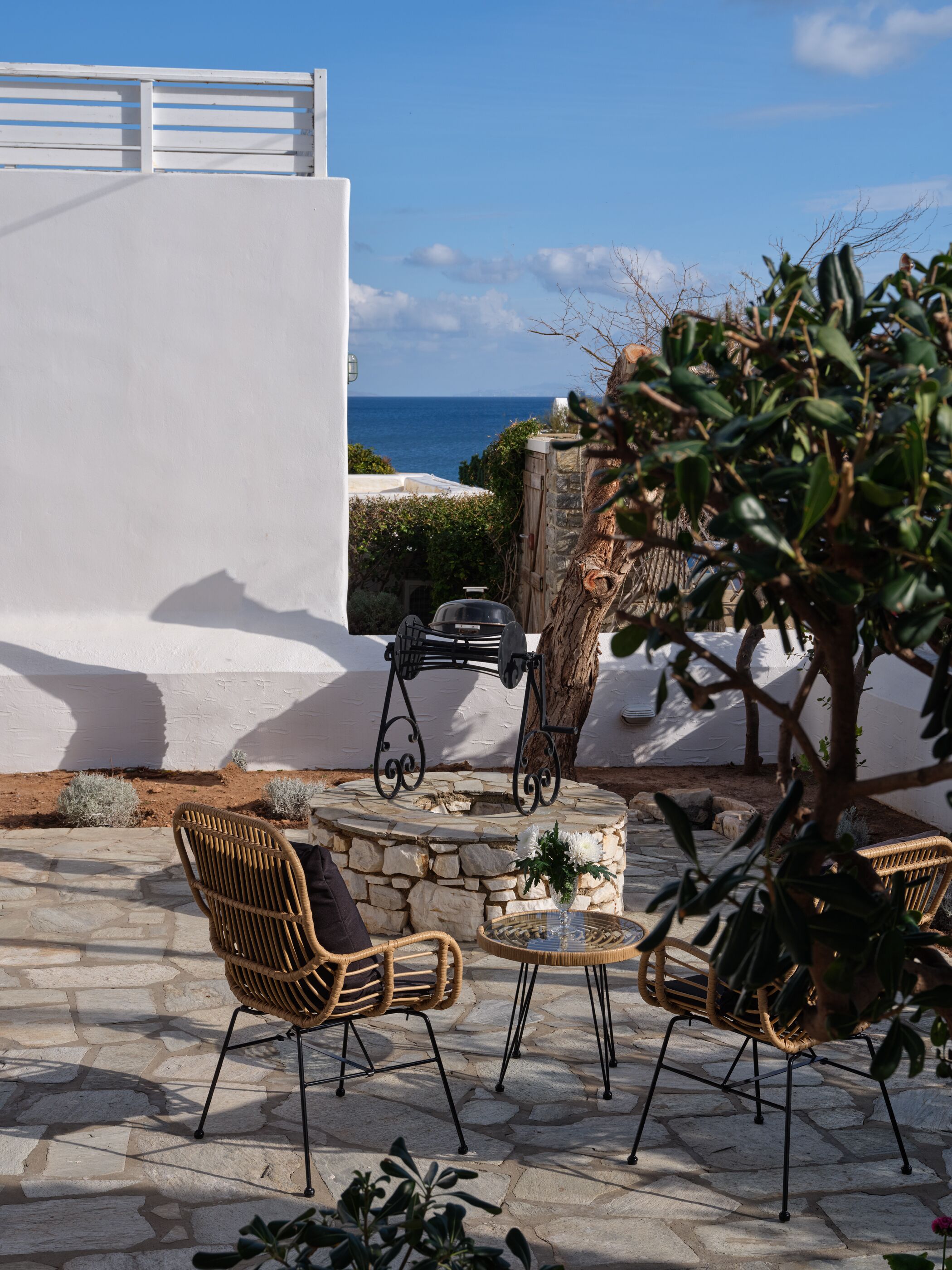 Une terrasse extérieure aménagée avec des meubles en osier, une table en pierre et un barbecue.