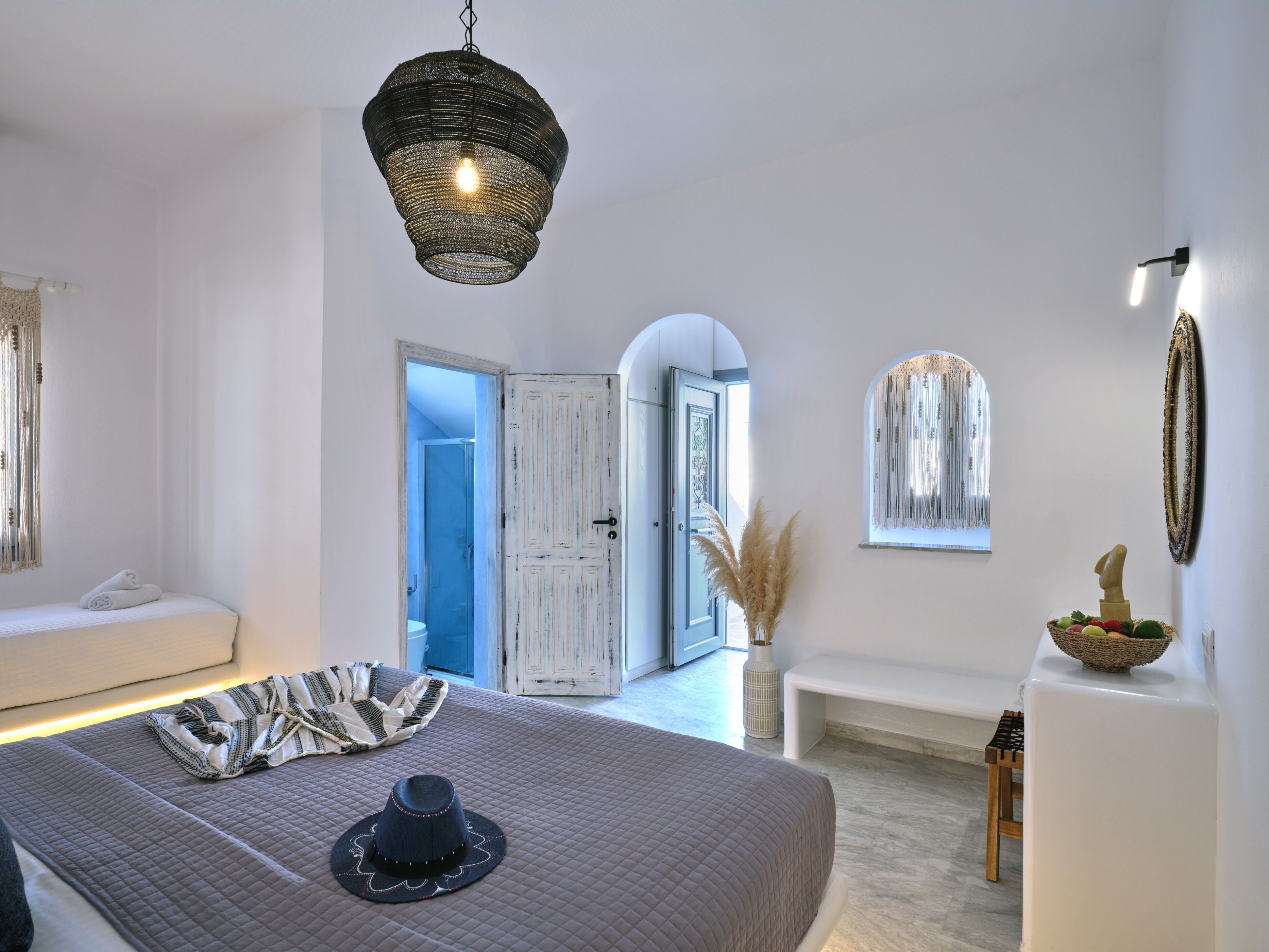 Un dormitorio con una cama, un candelabro, un banco y una puerta que da a otra habitación.