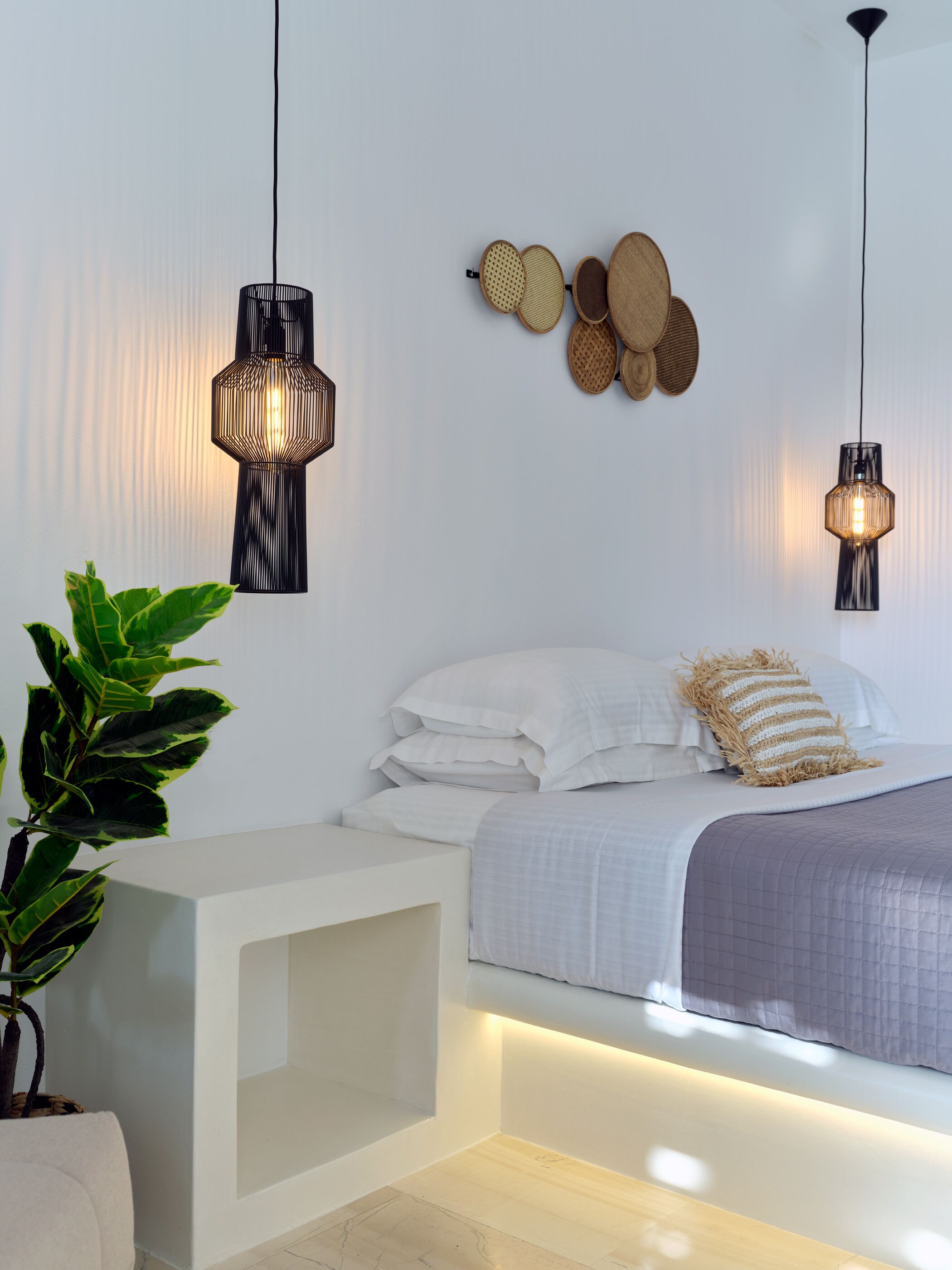 A modern bedroom with a bed, bedside tables, a potted plant, and two pendant lights.