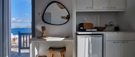 Una cocina moderna con armarios blancos, un taburete de madera, un fregadero y vistas al mar desde una puerta abierta.