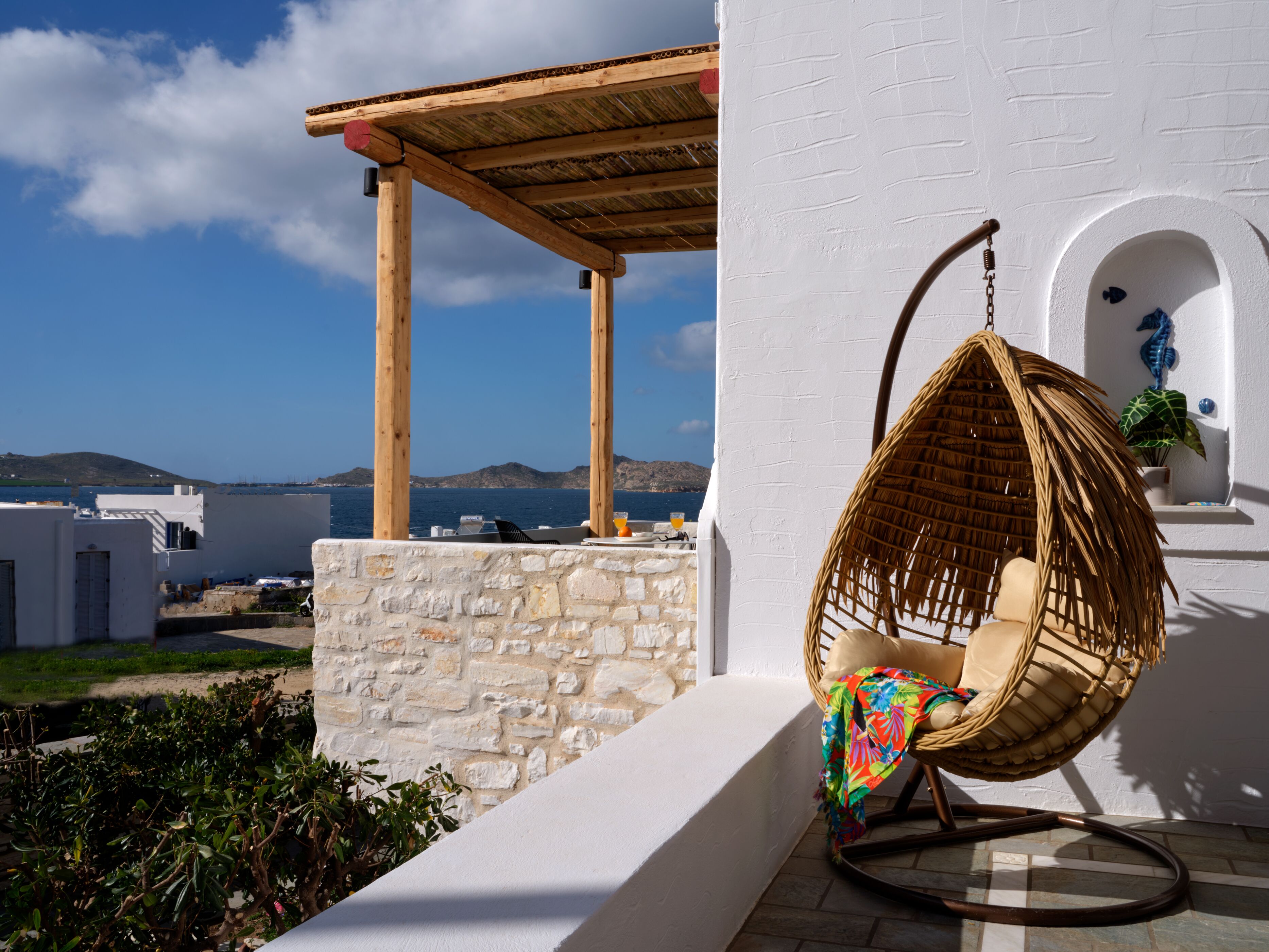 A wicker chair on a balcony with a view of the sea and hills.