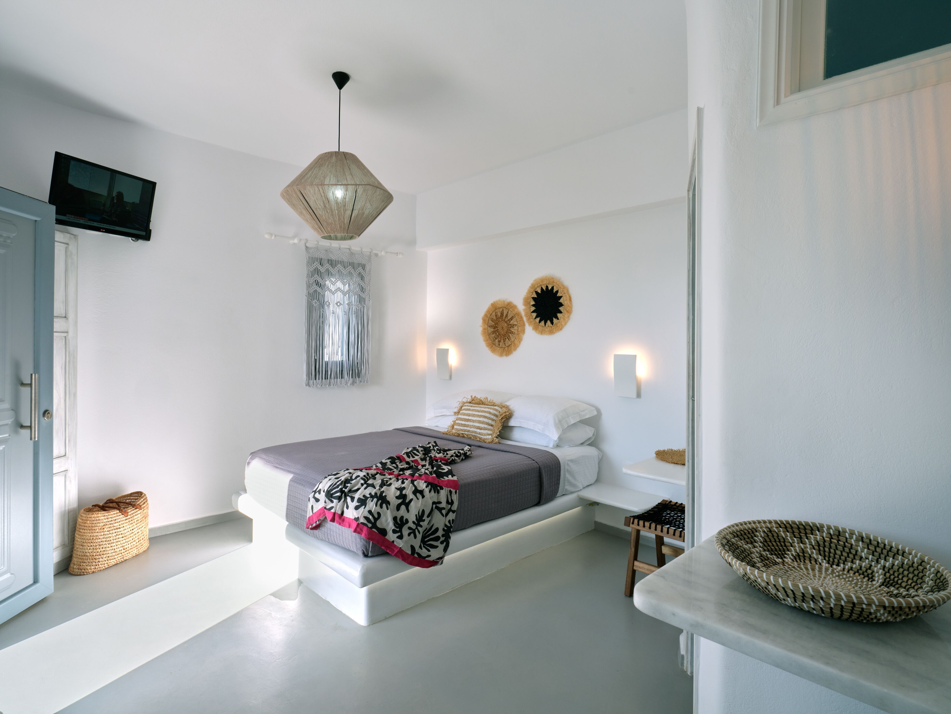A modern bedroom with a bed, bedside tables, a hanging light fixture, wall decor, and a television on the wall.