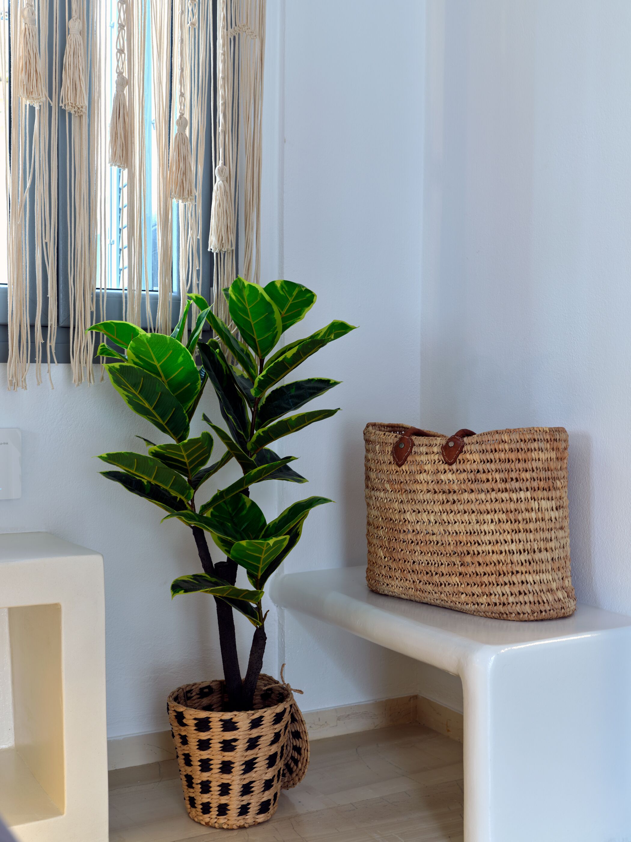 A room with a potted plant, a woven basket, and a macrame wall hanging.