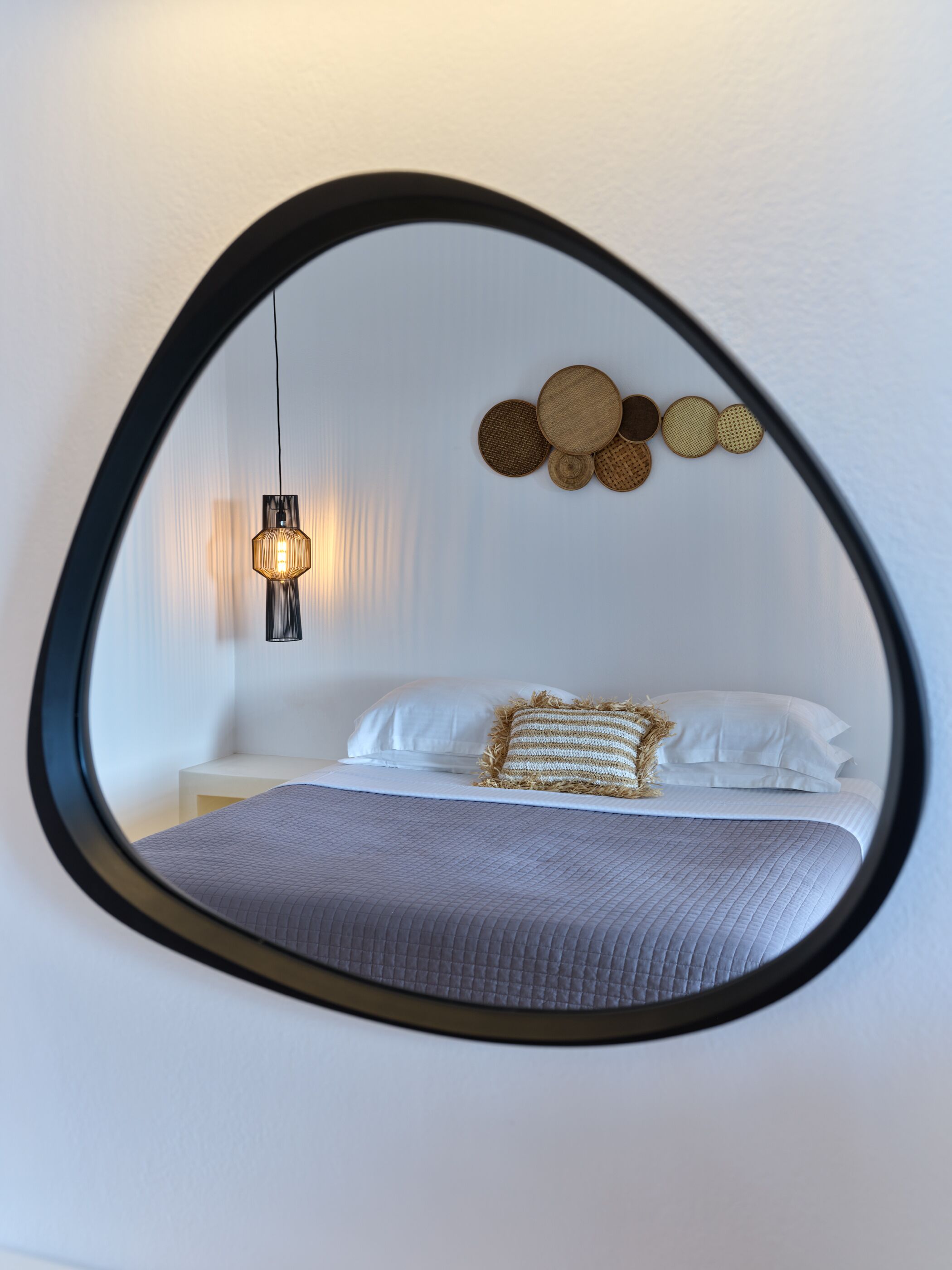 A bedroom with a bed, pillows, a hanging light fixture, and a wall-mounted mirror.