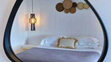 A bedroom with a bed, pillows, a hanging light fixture, and a wall-mounted mirror.