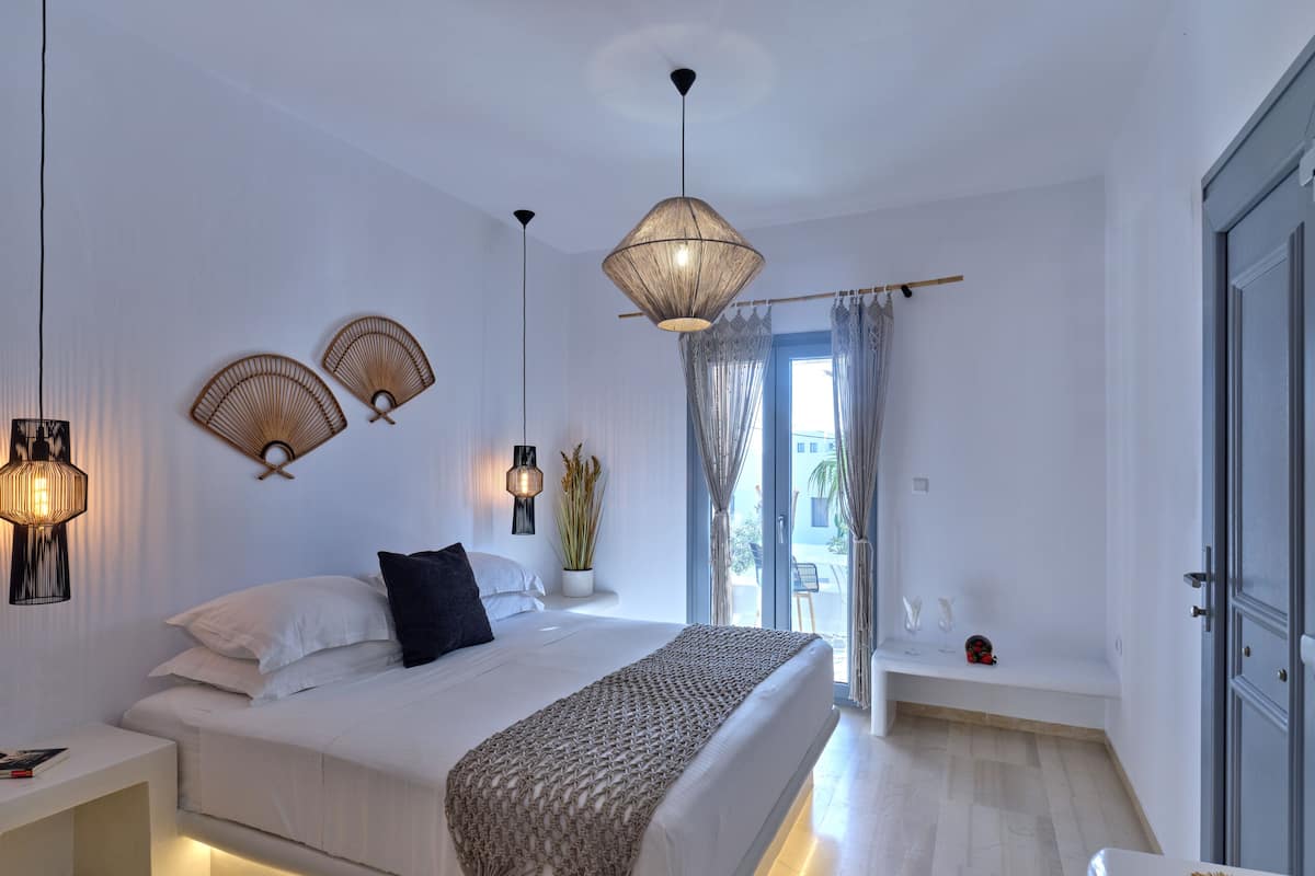 A modern bedroom with a large bed, bedside tables, a hanging light fixture, and a view of the outdoors.