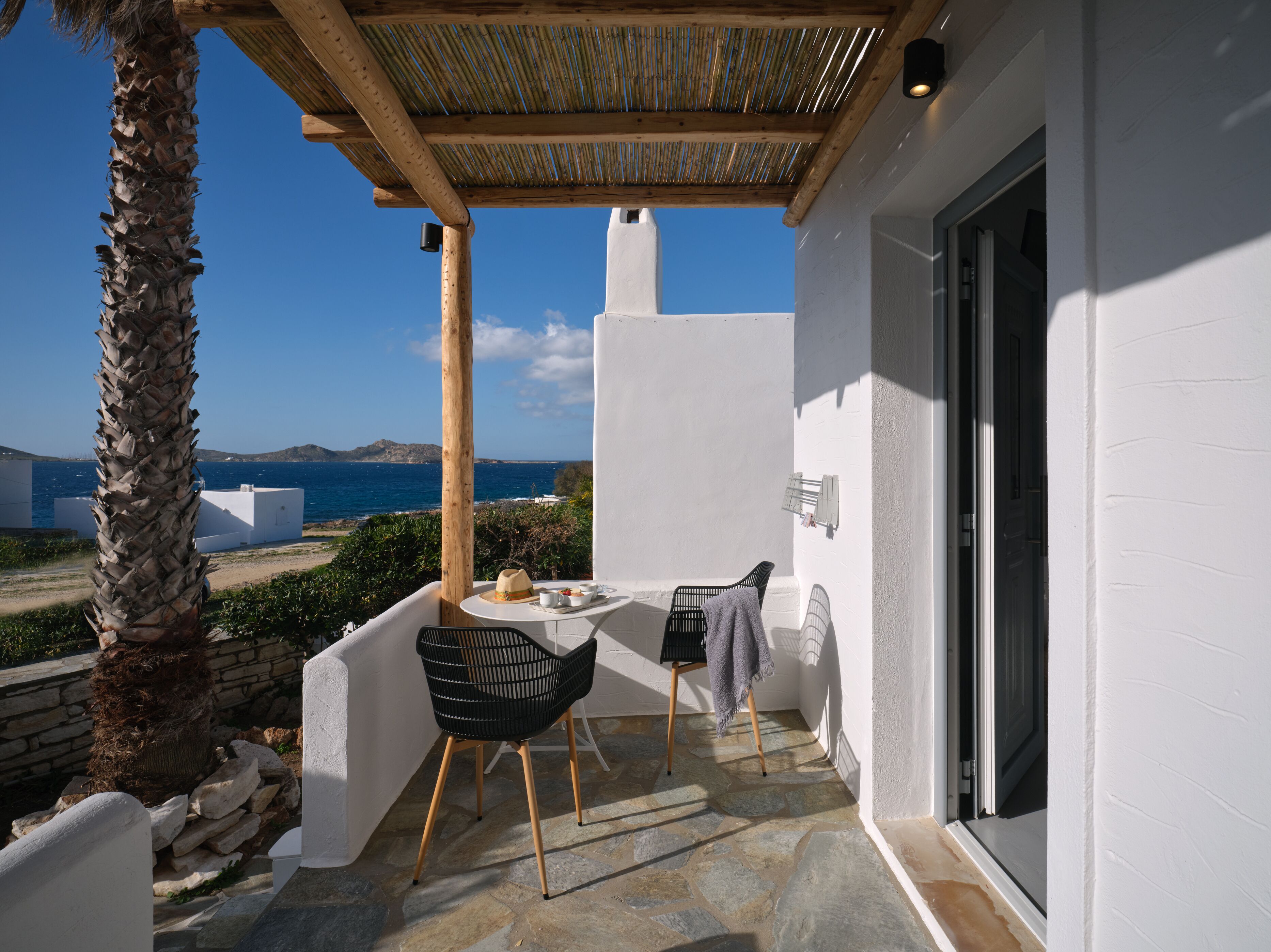 A balcony with a table and chairs, a view of the sea, and a white building.
