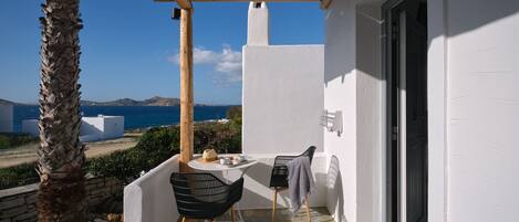 A balcony with a table and chairs, a view of the sea, and a white building.