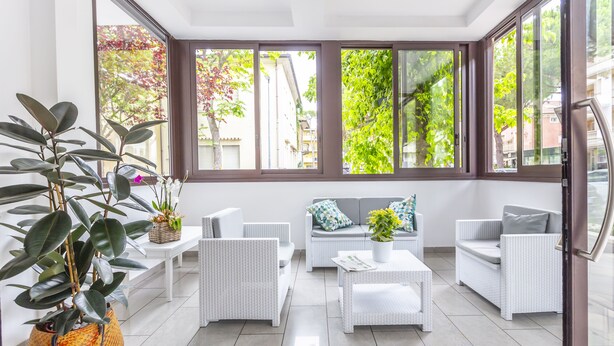 A bright, sunlit room with white wicker furniture, large windows, and a potted plant. - Hotel Luana  (Riccione)