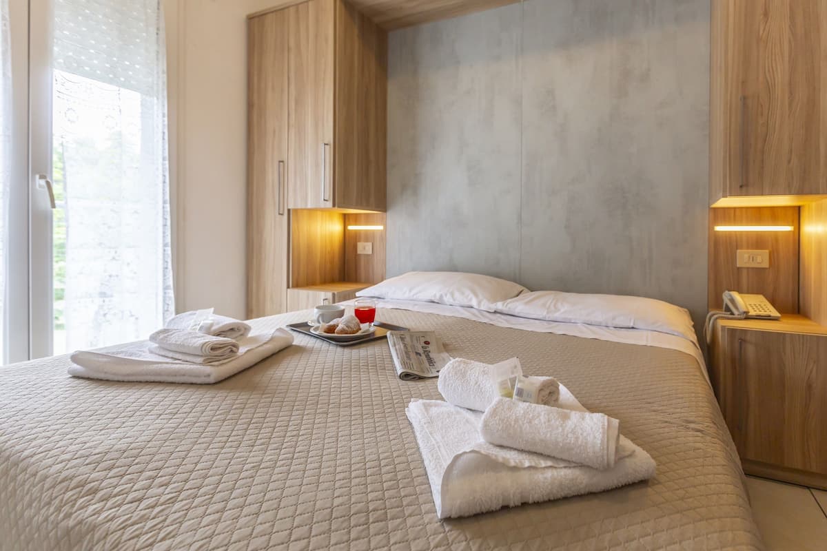 A neatly made bed with towels, a tray with pastries and a drink, and a remote control on a wooden nightstand.