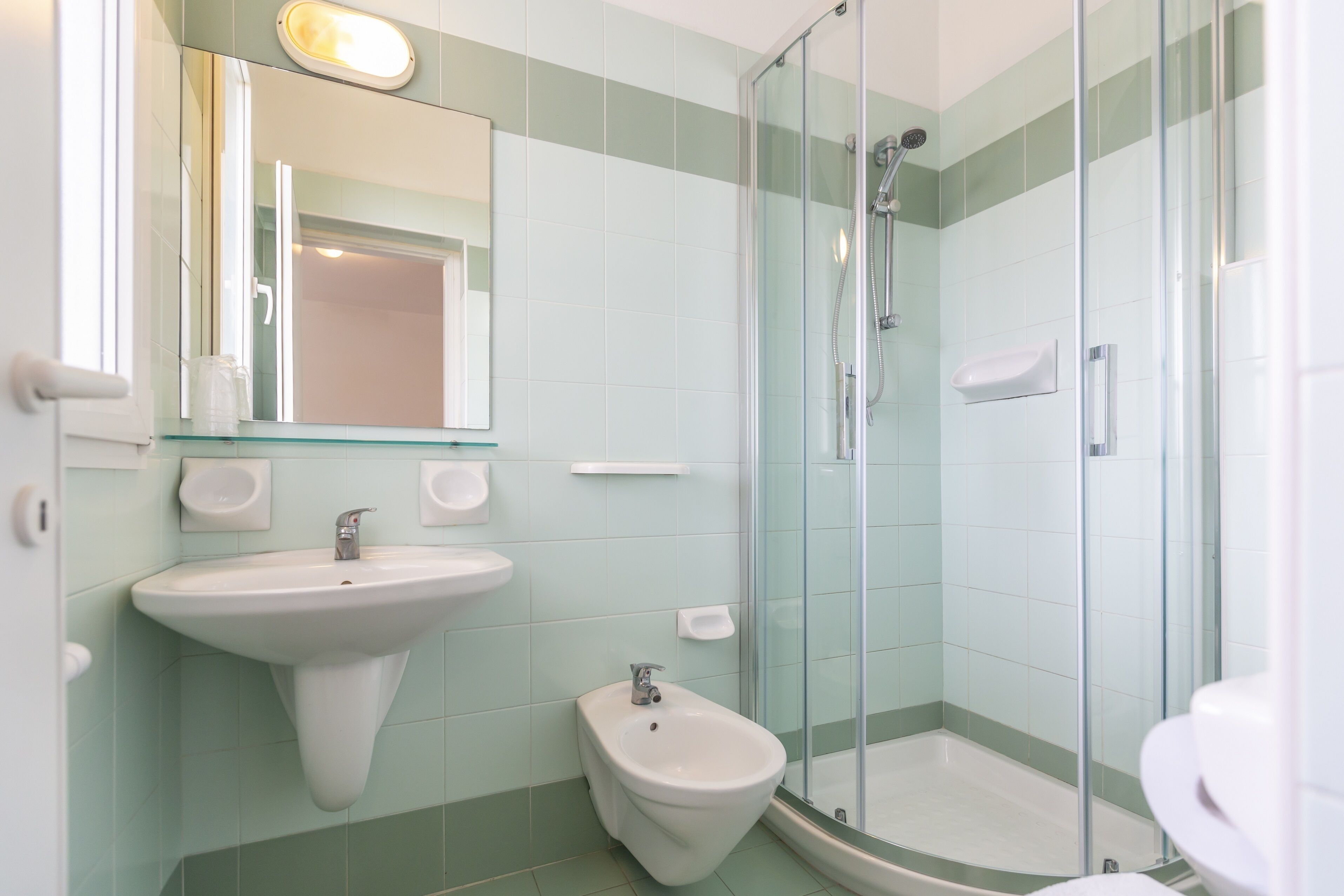 A bathroom with a glass-enclosed shower, a pedestal sink, and a bidet.