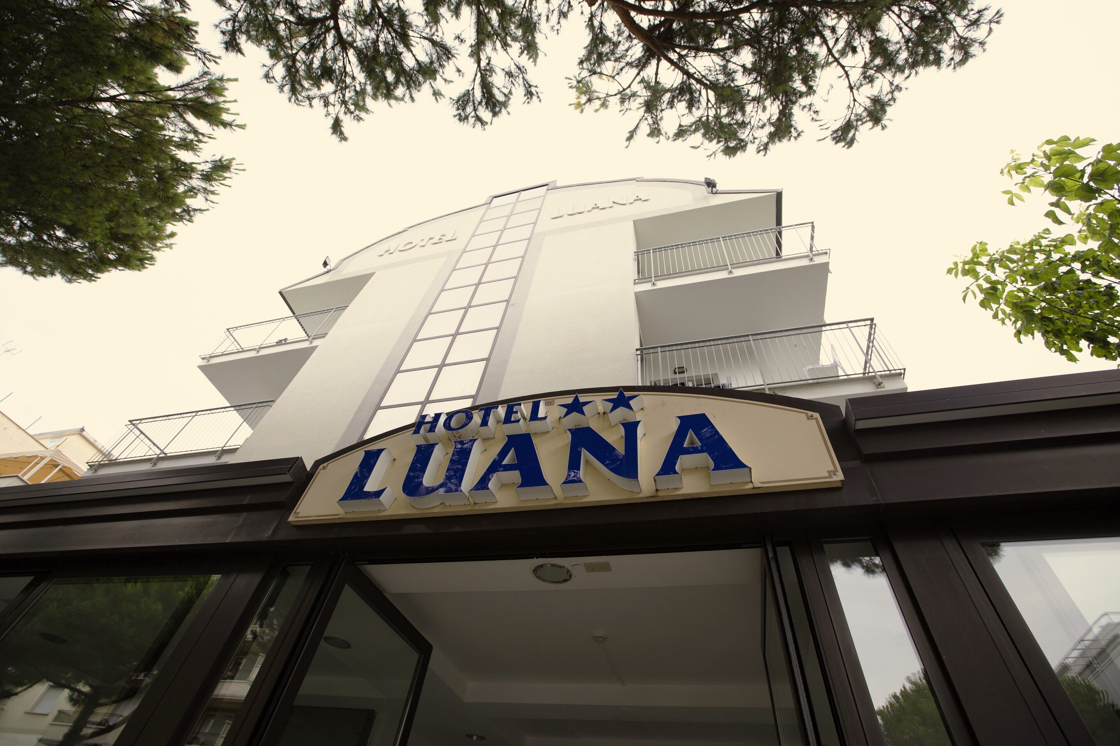 The exterior of Hotel Luana with a prominent sign and a modern architectural design.