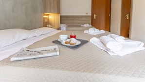 A hotel room with two beds, a tray with pastries, a newspaper, and towels. - Hotel Luana  (Riccione)