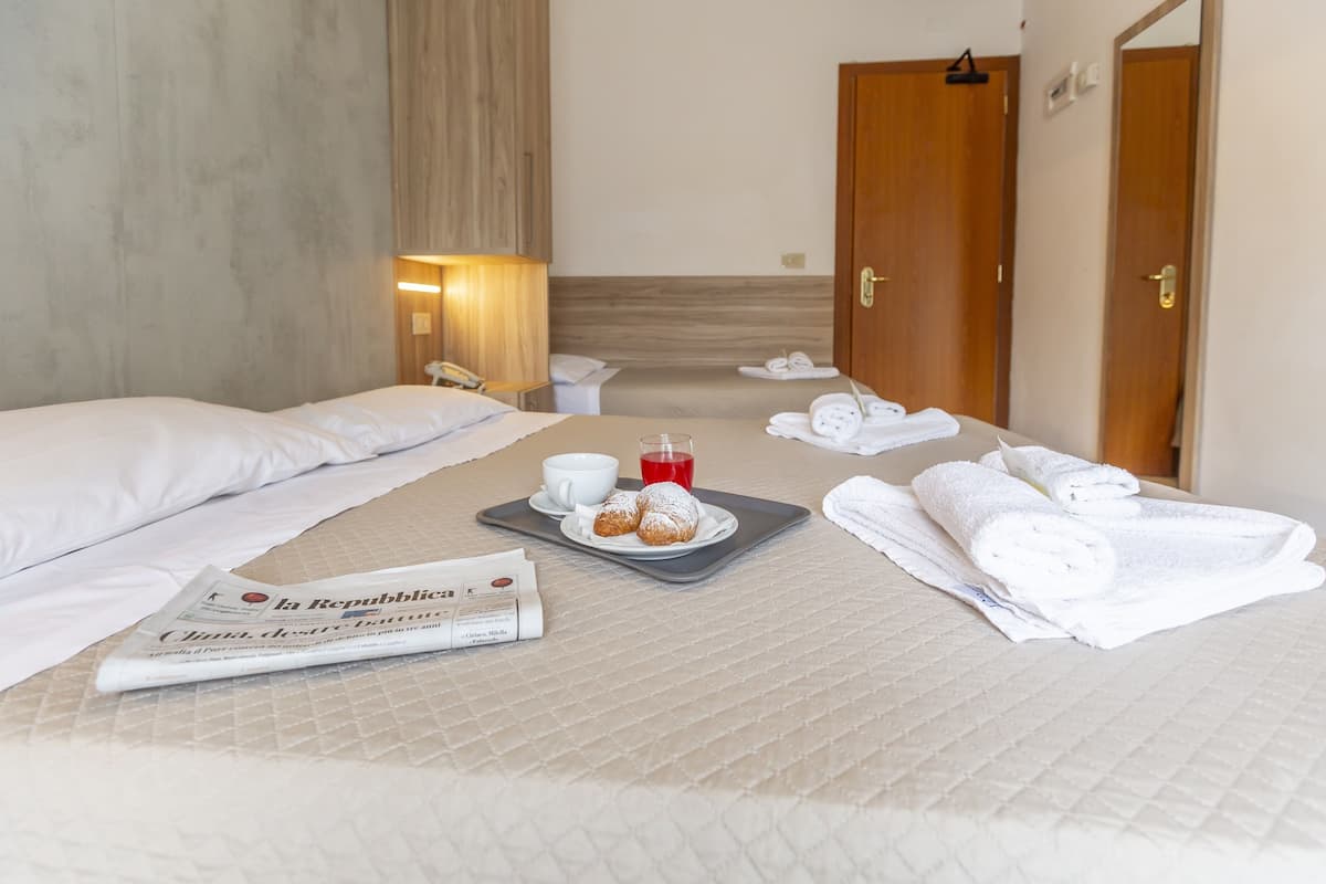 A hotel room with two beds, a tray with pastries, a newspaper, and towels.