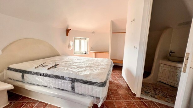 Un dormitorio con cama, mesita de noche, ventana y un baño visible a través de una puerta abierta.