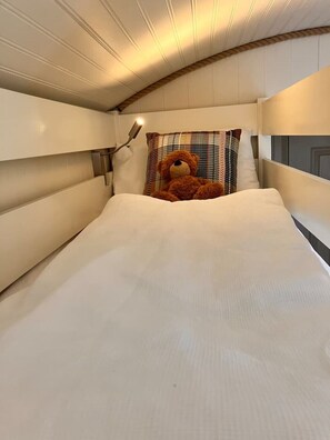 Ein Bett mit Teddybär, Lampe und kariertem Kopfkissen.